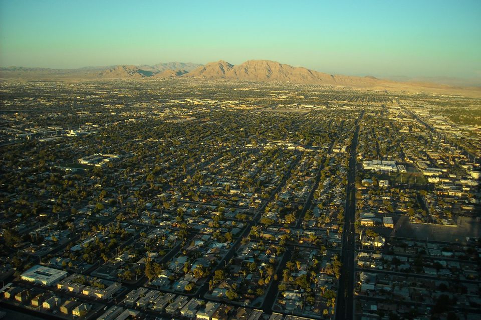 An aerial photo of the Vegas suburbs taken in the late afternoon, with mountains and the desert sky in the background.